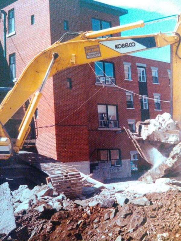 Une excavatrice Kobelco creuse un trou devant un bâtiment en brique