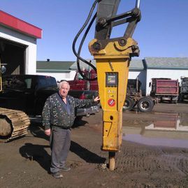 Un homme se tient à côté d’une grosse machine jaune dans un parking.