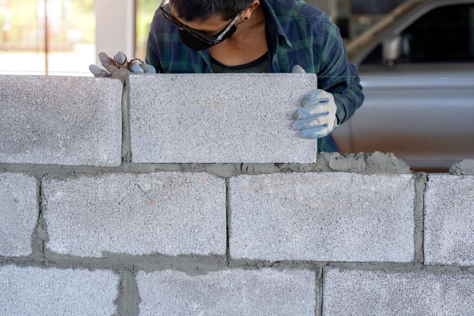 Person wearing safety glasses and gloves, laying concrete blocks, outdoors.