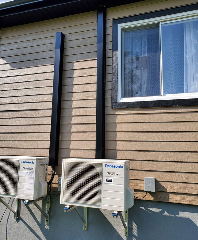 Deux unités de climatisation extérieures Panasonic, installées sur la façade d'une maison, sous une fenêtre.