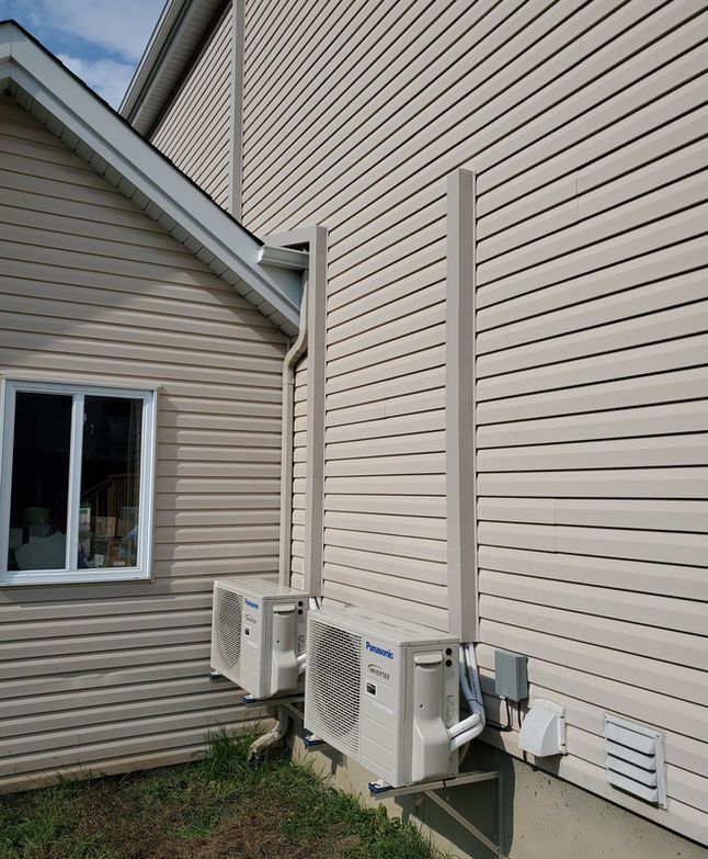 Extérieur de maison beige avec deux climatiseurs muraux de part et d'autre d'une fenêtre et des conduits d'aération.