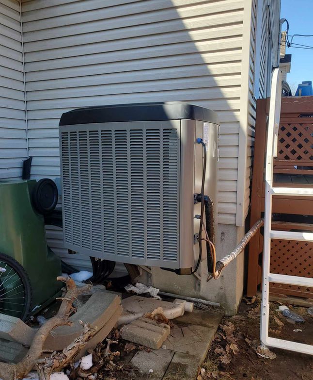 Unité de climatisation extérieure à côté d'une maison, avec des débris éparpillés au sol.