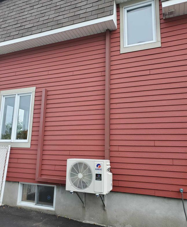 Maison à façade rouge, fenêtre blanche et unité de climatisation extérieure sur fondations en béton.