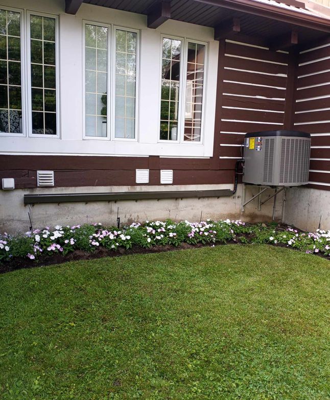 Extérieur de la maison avec fenêtres blanches, bardage marron, parterre de fleurs et pelouse verte