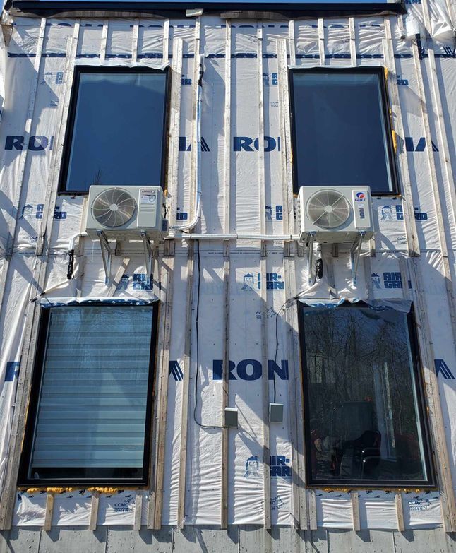 Quatre fenêtres et deux climatiseurs sur une façade blanche à bardage métallique.