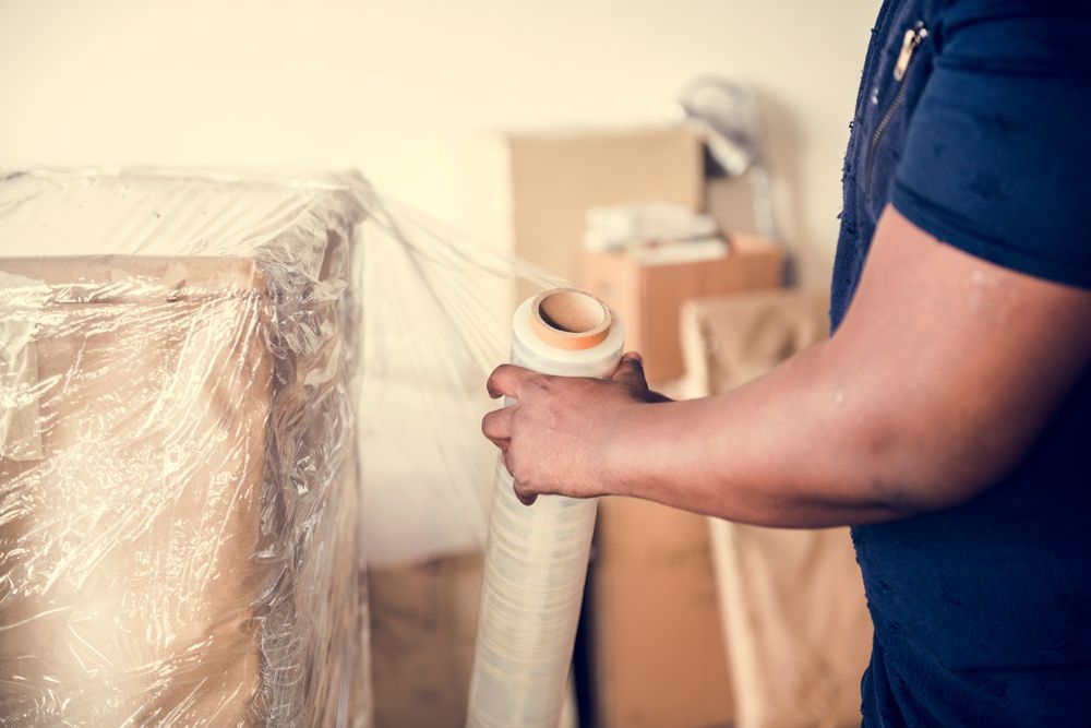 Person Wrapping Furniture With Clear Plastic Wrap — JR Removals Mackay in Moranbah, QLD