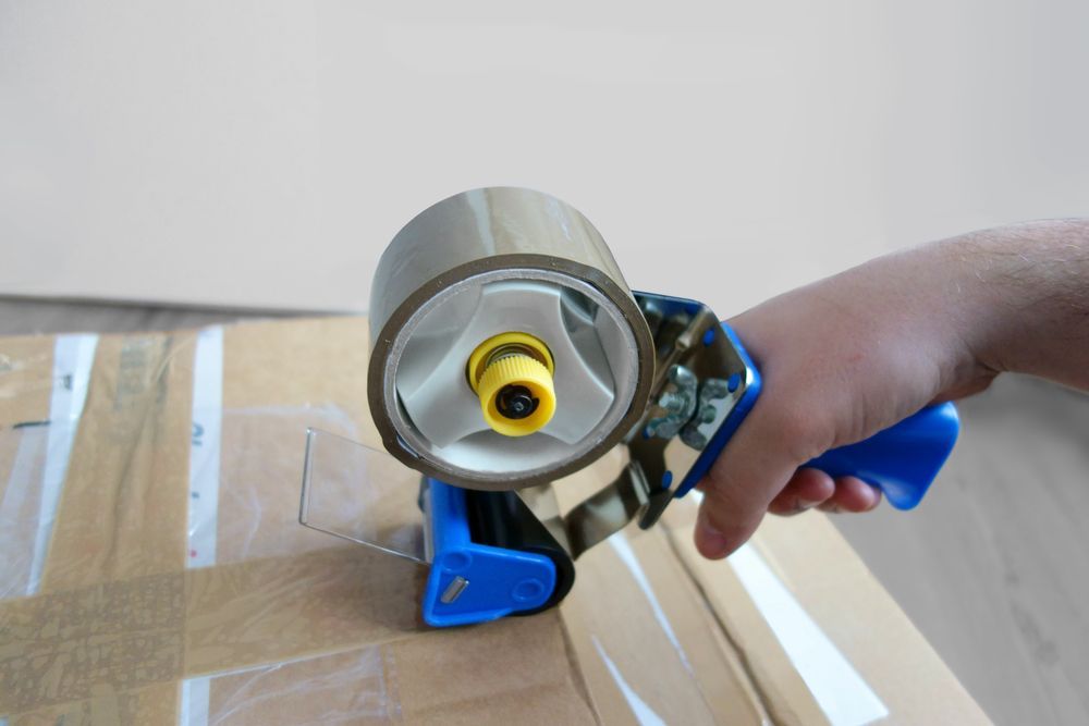 Hand Using a Blue Packing Tap — JR Removals Mackay in Bucasia, QLD