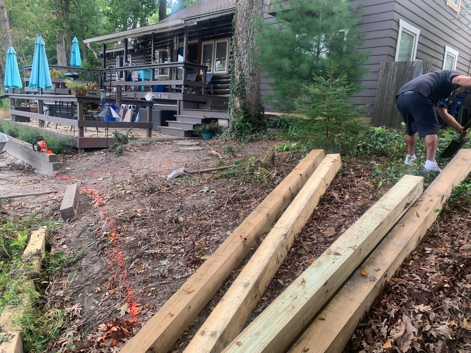 Two men working on a wooden construction project in front of a house. Lumber and tools present.