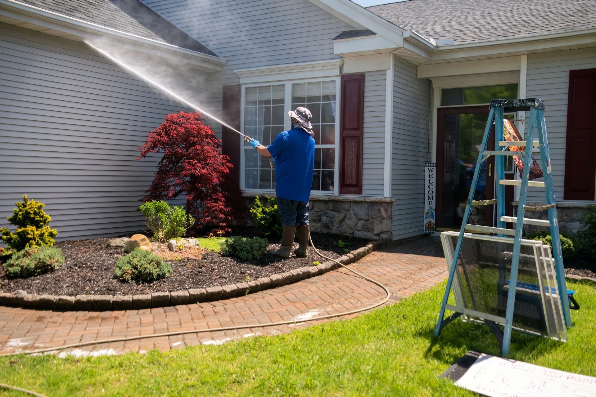 Person power washing siding of a house with red shutters.