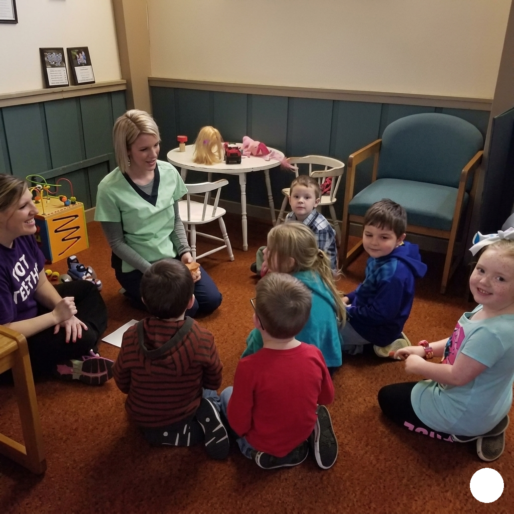 Children and two adults sit in a circle on the floor in a cozy room, listening during story time.