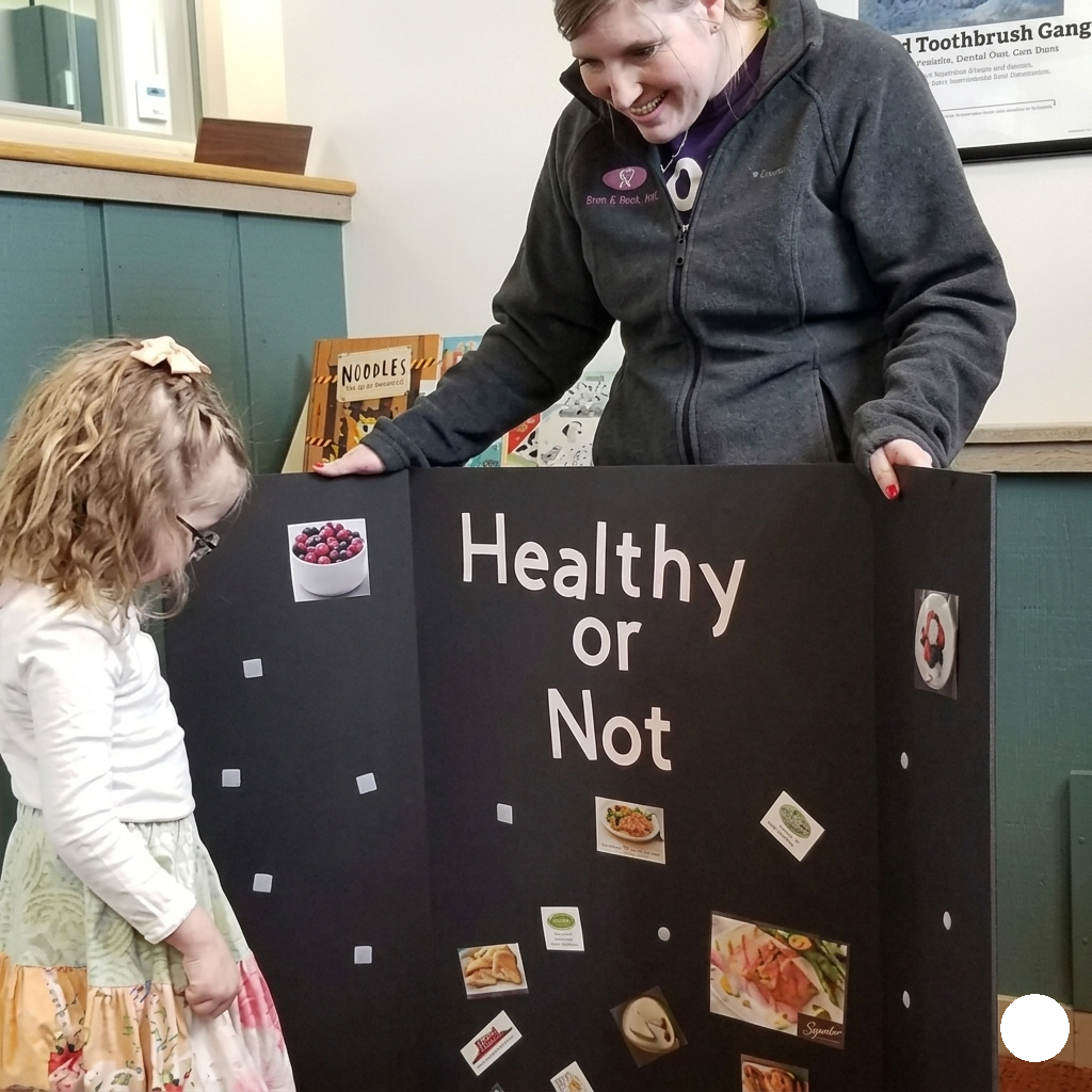 Two people standing by a black board labeled “Healthy or Not” with food pictures on it.
