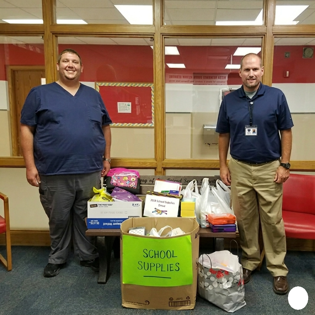 Two men stand beside boxes of school supplies in a hallway
