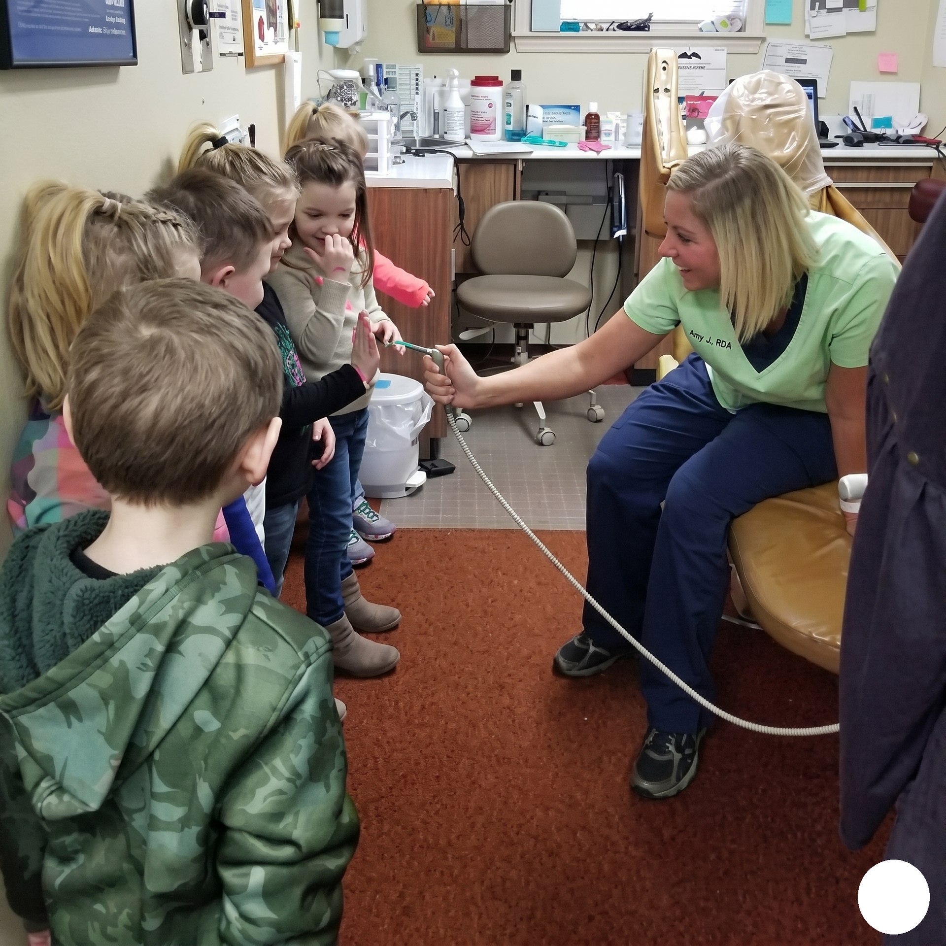Children in a waiting room feed a patient seated on a couch with a bottle and tube.
