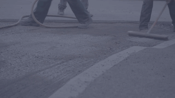 Workers smoothing freshly laid asphalt on a road, using hoses and a squeegee.