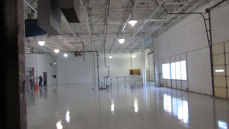 Bright, empty industrial space with reflective floor, overhead lights, and garage door.