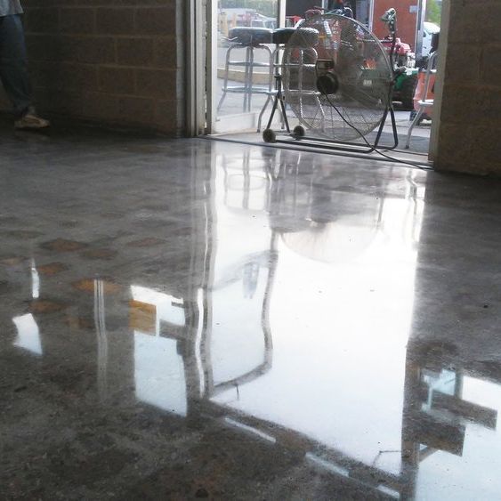 Polished concrete floor reflecting a bright light and a view of the outside through an open doorway.