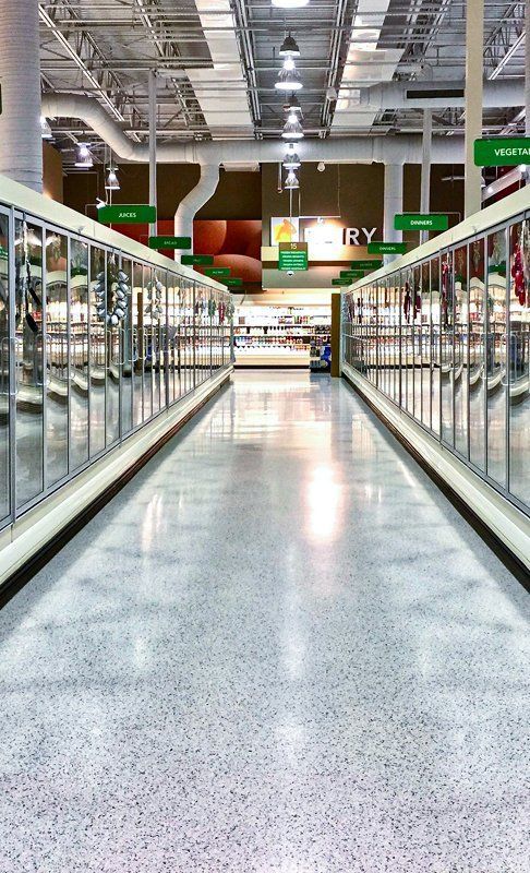 Interior grocery store aisle with freezer cases on either side, leading to a blurry background.