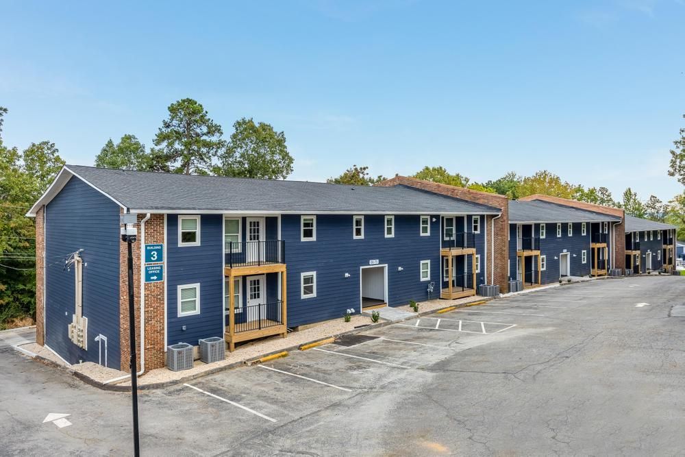 A blue apartment building with a parking lot in front of it.