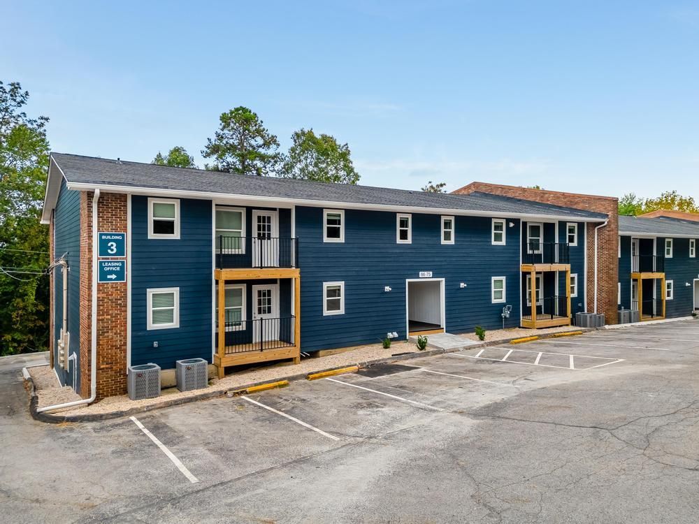 A blue apartment building with a parking lot in front of it.