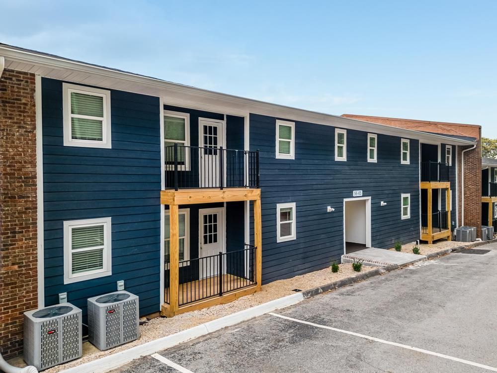 A blue apartment building with a lot of windows and a parking lot in front of it.