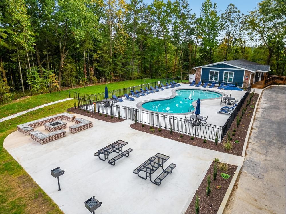 An aerial view of a swimming pool with tables and chairs and a fire pit.