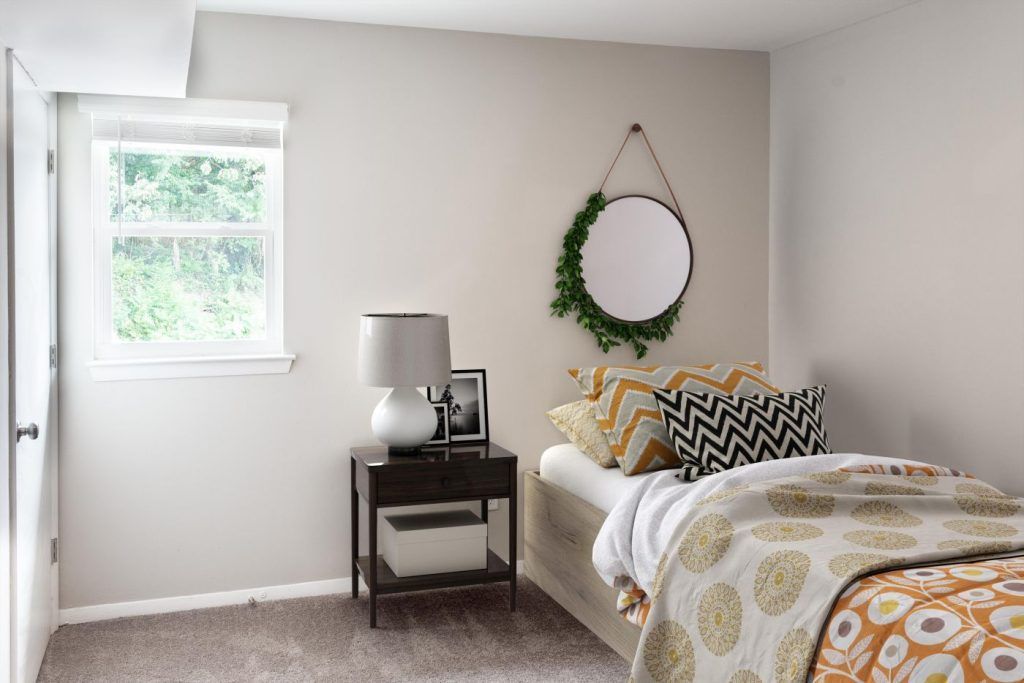 A bedroom with a bed, nightstand, lamp and mirror.