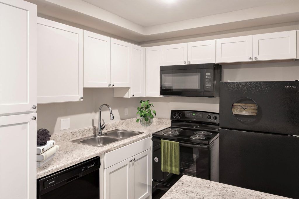 A kitchen with white cabinets, black appliances, a sink, stove, microwave, and refrigerator.