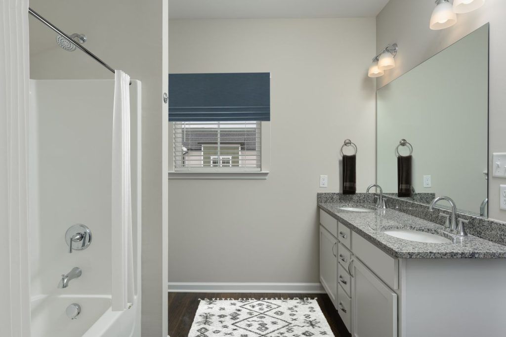 A bathroom with a tub, sink, mirror and window.
