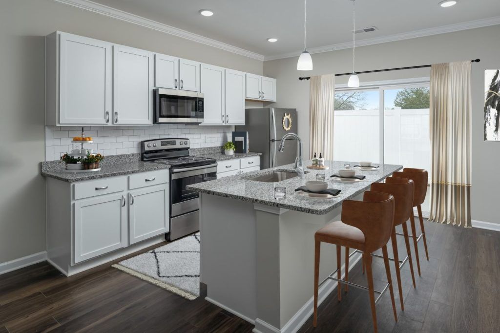 A kitchen with white cabinets, granite counter tops, stainless steel appliances, and a large island.