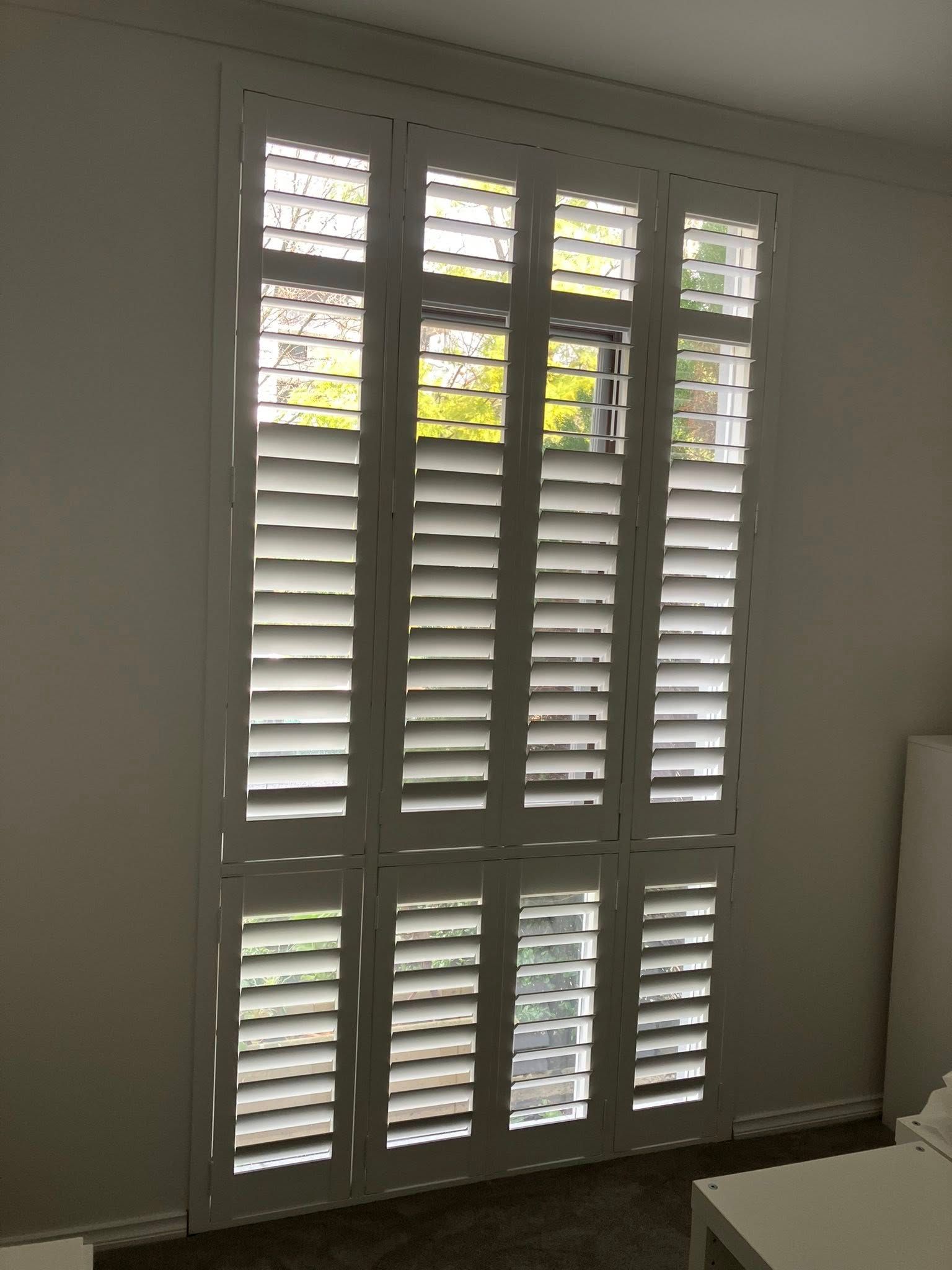 White plantation shutters on a window with daylight filtering through.