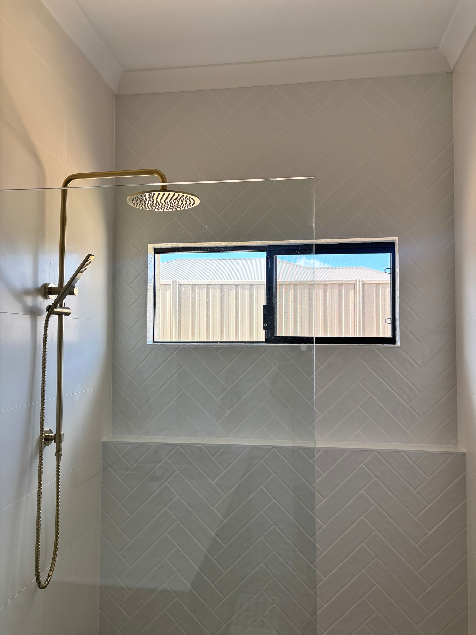 Plantation shutters installed in a living room with black recliner, wall poster, windows, and bubble wrap on the carpet in Perth, WA.