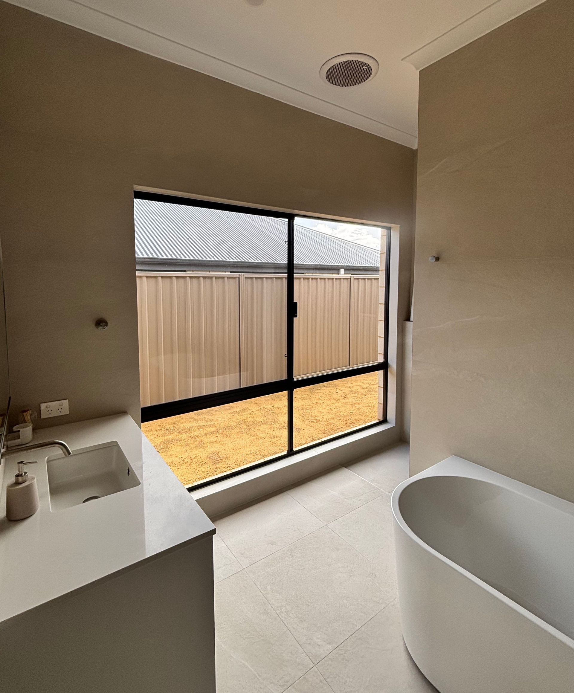 Plantation shutters installed in a minimal bedroom with a round window, slanted ceiling, bed, and small step ladder in Joondalup, WA.