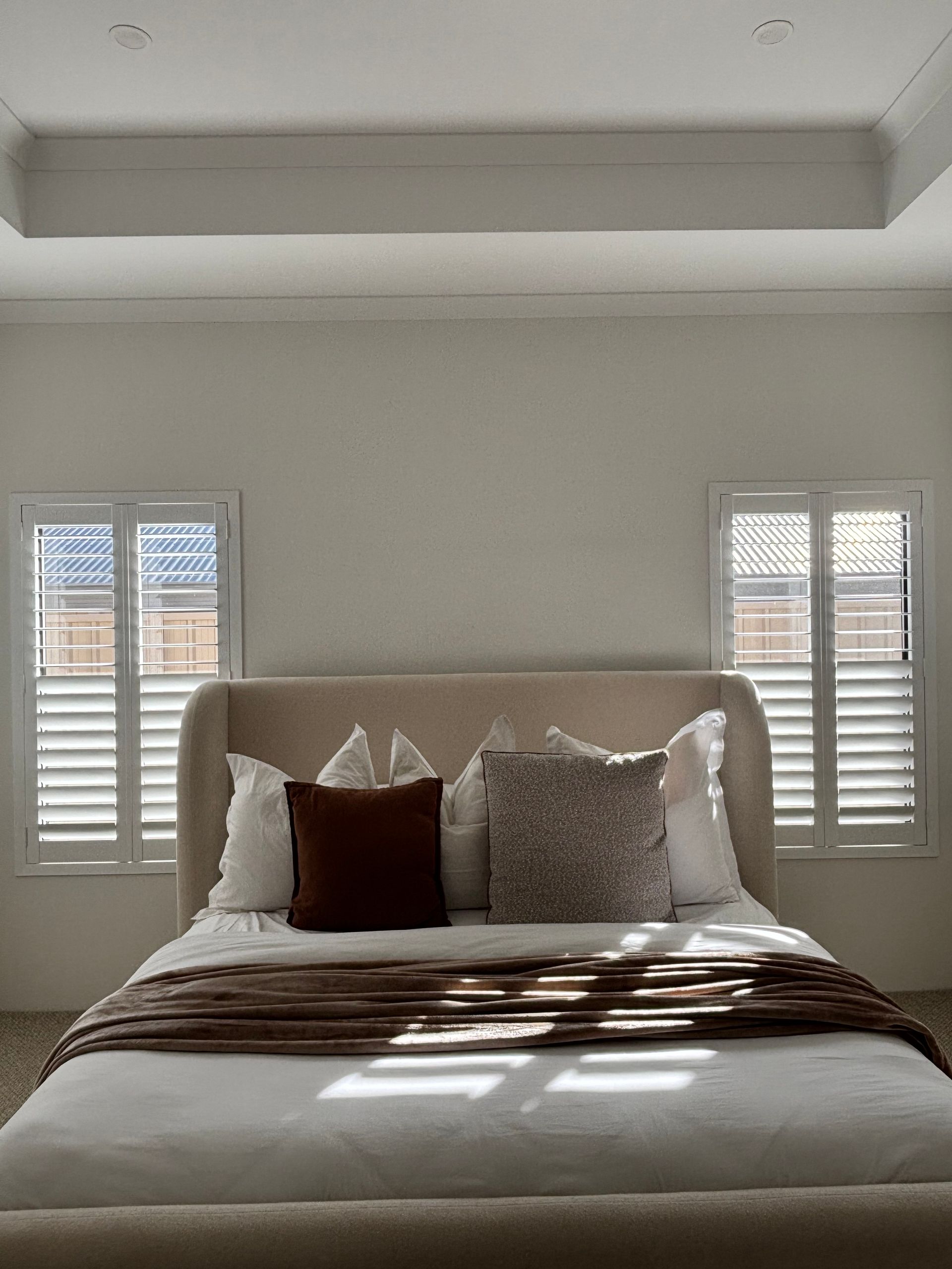 Plantation shutters installed in a white louvered cabinet with glass doors and shelves in a room with hardwood floors in Joondalup, WA.