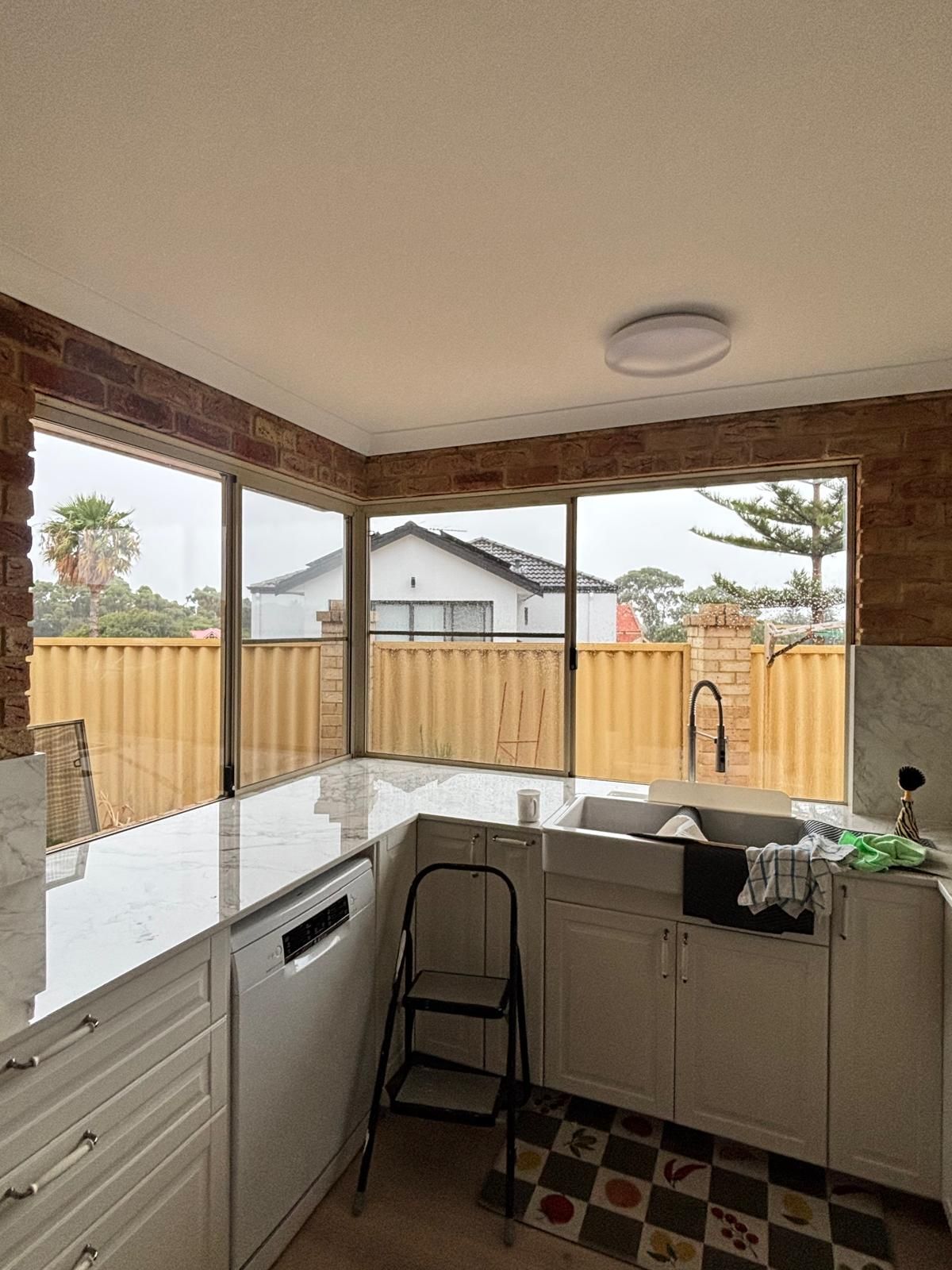 Plantation shutters installed in a sunlit bathroom with a corner tub and large windows overlooking trees and distant city buildings in Joondalup, WA.