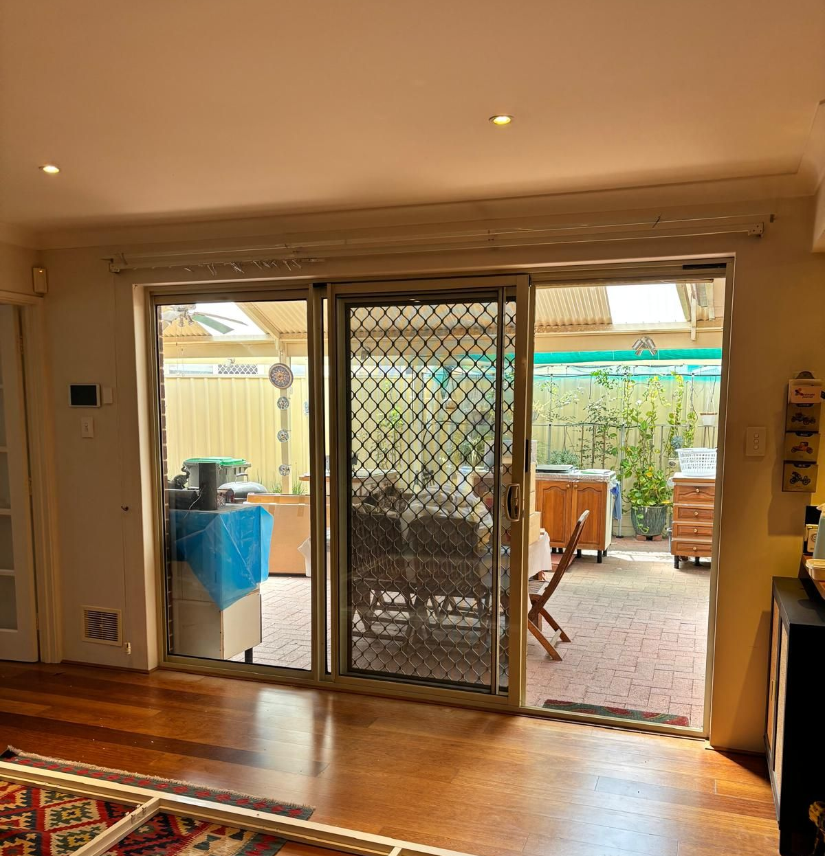 Plantation shutters installed in a bright sunroom with glass doors opening to a turquoise pool and patio, with a table in the foreground in Perth, WA.
