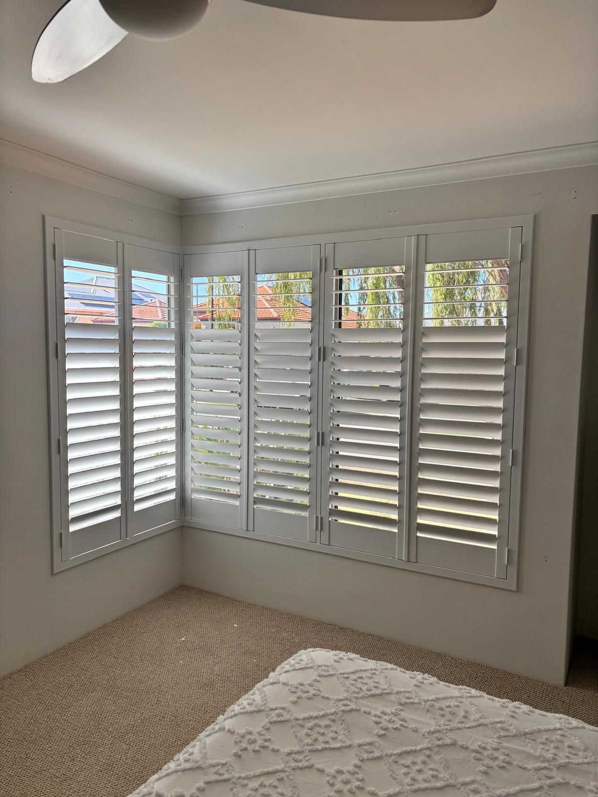 Plantation shutters installed in an empty room with dark wood floors, white plantation shutters, and recessed ceiling lights in Joondalup, WA.
