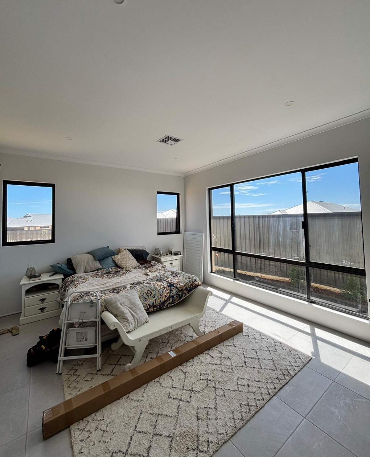Plantation shutters installed in a living room couch facing bright bay windows with a colorful backyard view in Perth, WA.