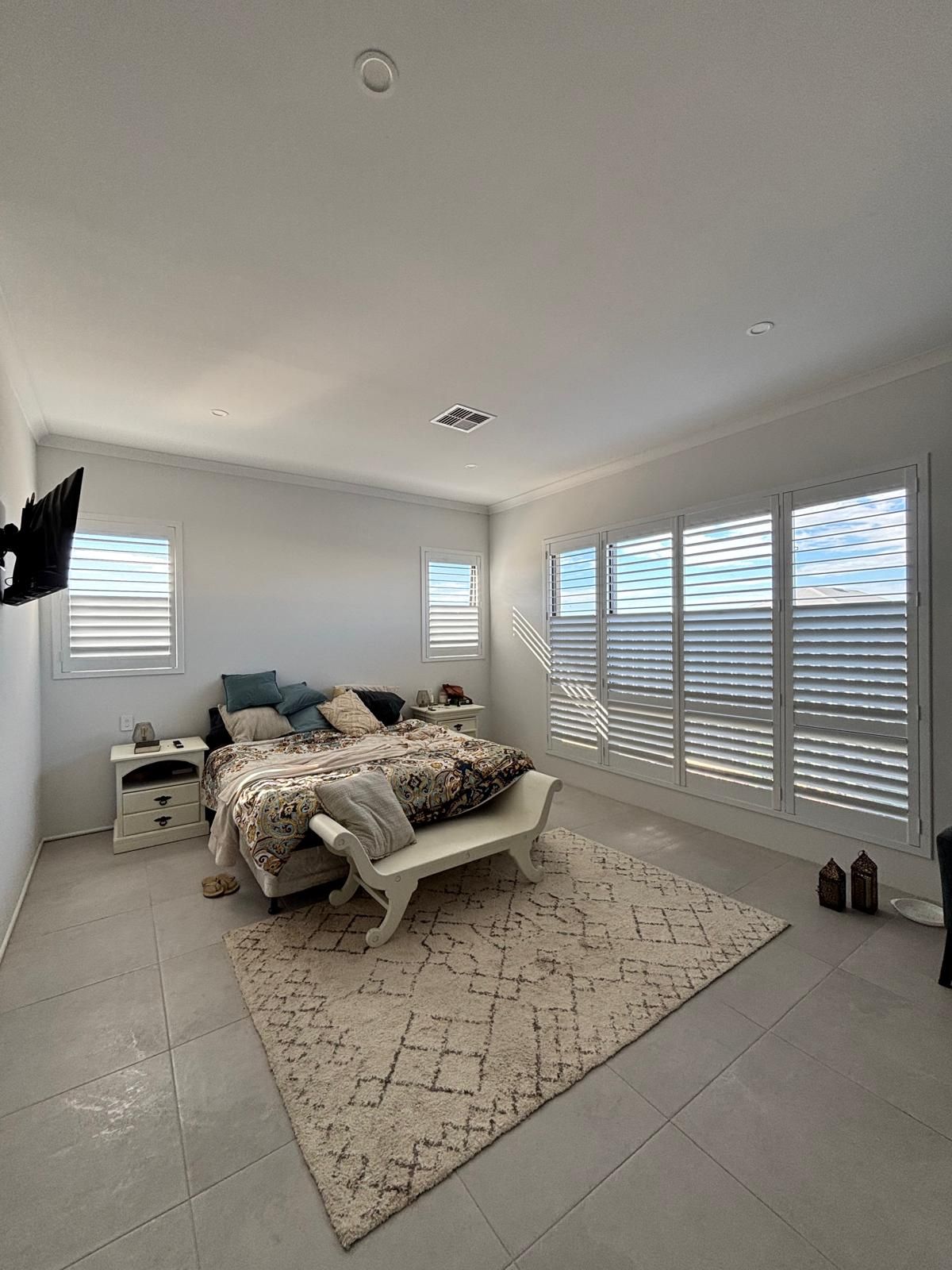 Plantation shutters installed in a living room with bay window shutters and a sofa covered in pillows in Perth, WA.