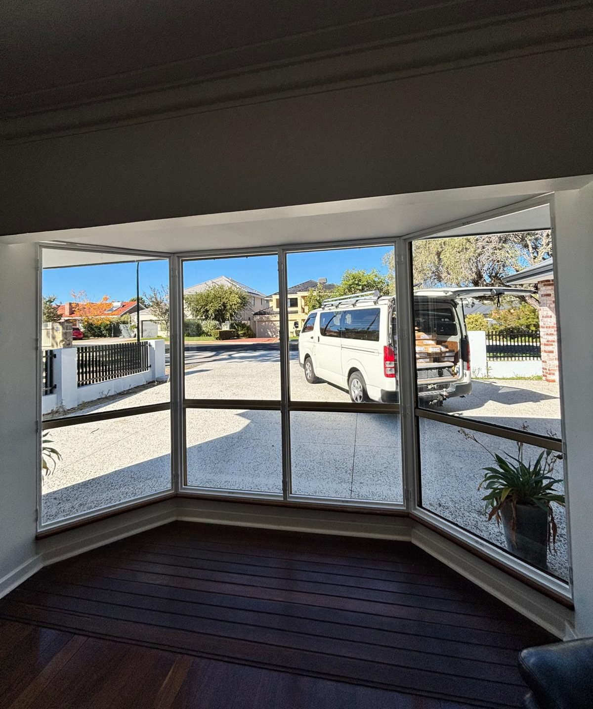 Plantation shutters installed in a sunlit bathroom with a corner tub and large windows overlooking trees and distant city buildings in Joondalup, WA.