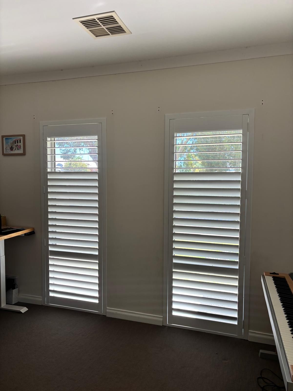 Plantation shutters installed in a white plantation shutters on a window with a blue sky and rooftops visible through the slats in Joondalup, WA.