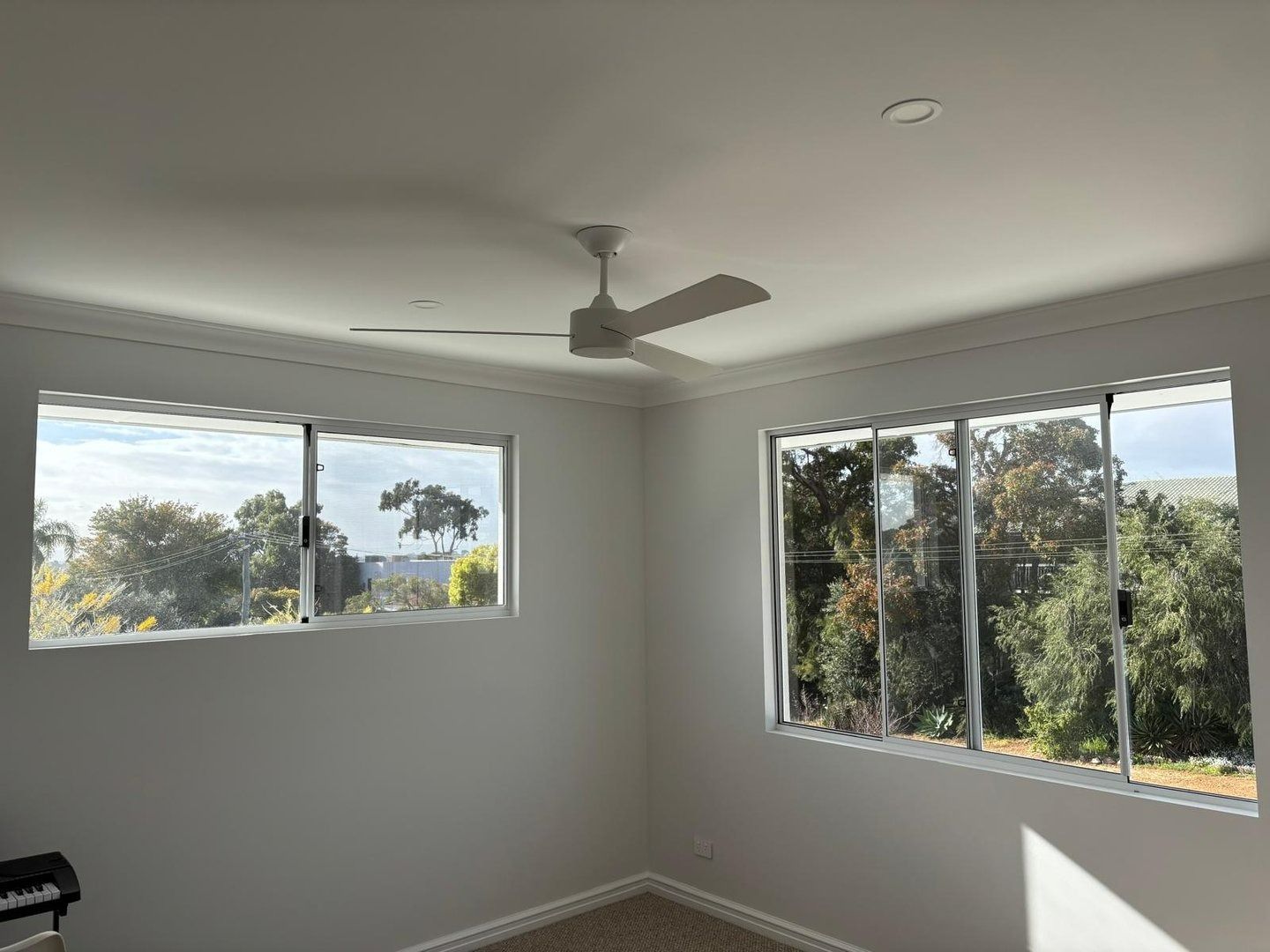 Plantation shutters installed in an empty white room with large windows, a ceiling fan, and trees visible outside in Joondalup, WA.
