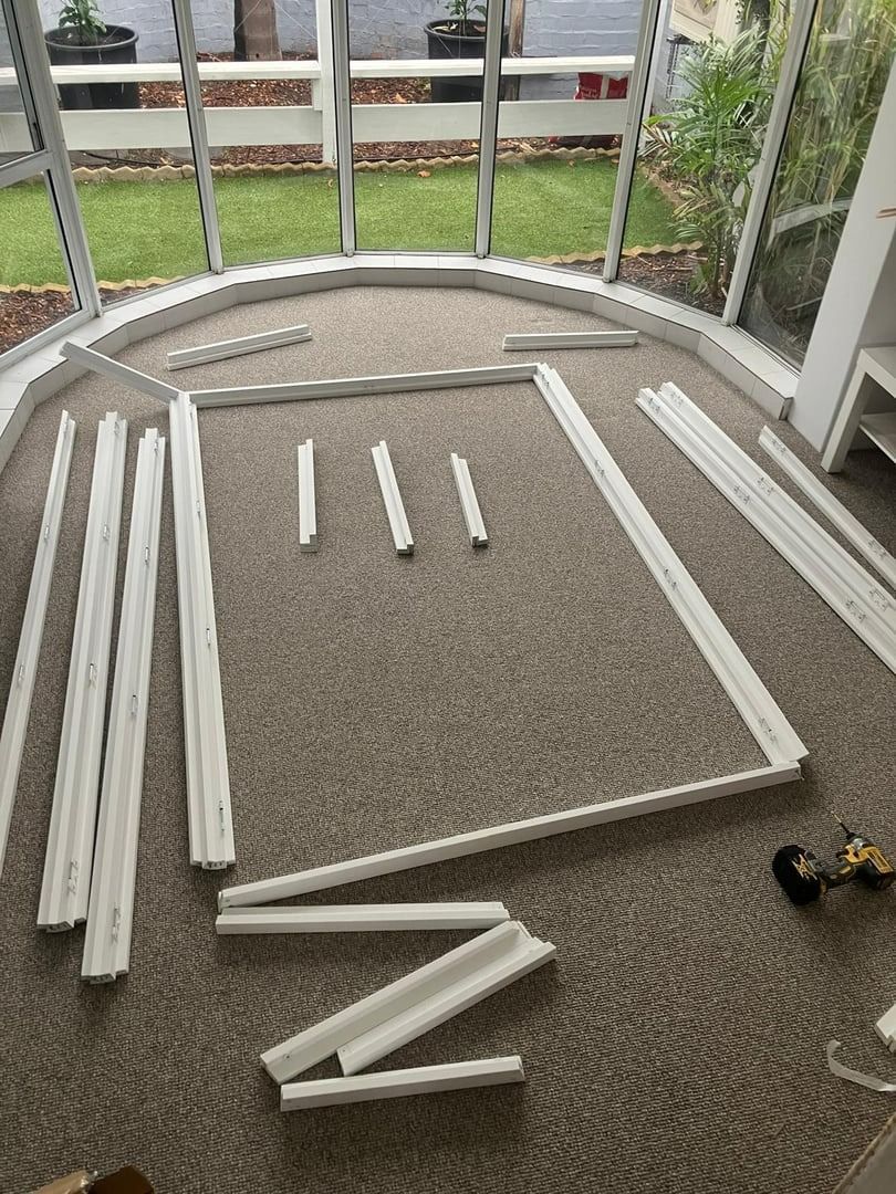 Plantation shutters installed in a white trim pieces laid out on a carpeted porch in a geometric frame, with a small drill nearby in Joondalup, WA.