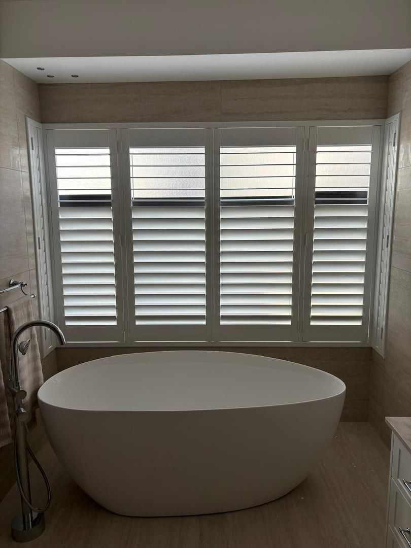 Plantation shutters installed in a modern bathroom with a freestanding oval tub in front of large white shutters in Perth, WA.