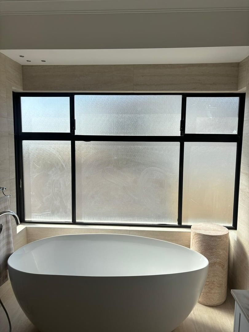 Plantation shutters installed in a modern bathroom with a freestanding white tub in front of frosted black-framed windows in Perth, WA.