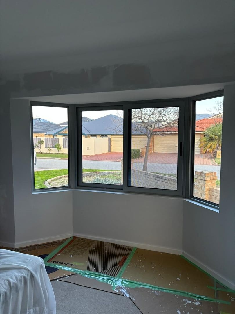 Plantation shutters installed in an empty living room with large bay windows overlooking a neighborhood street in Joondalup, WA.