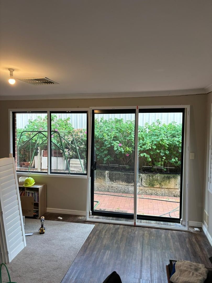 Plantation shutters installed in an empty living room with carpet, sliding glass doors, and a view of a leafy patio and fence in Perth, WA.