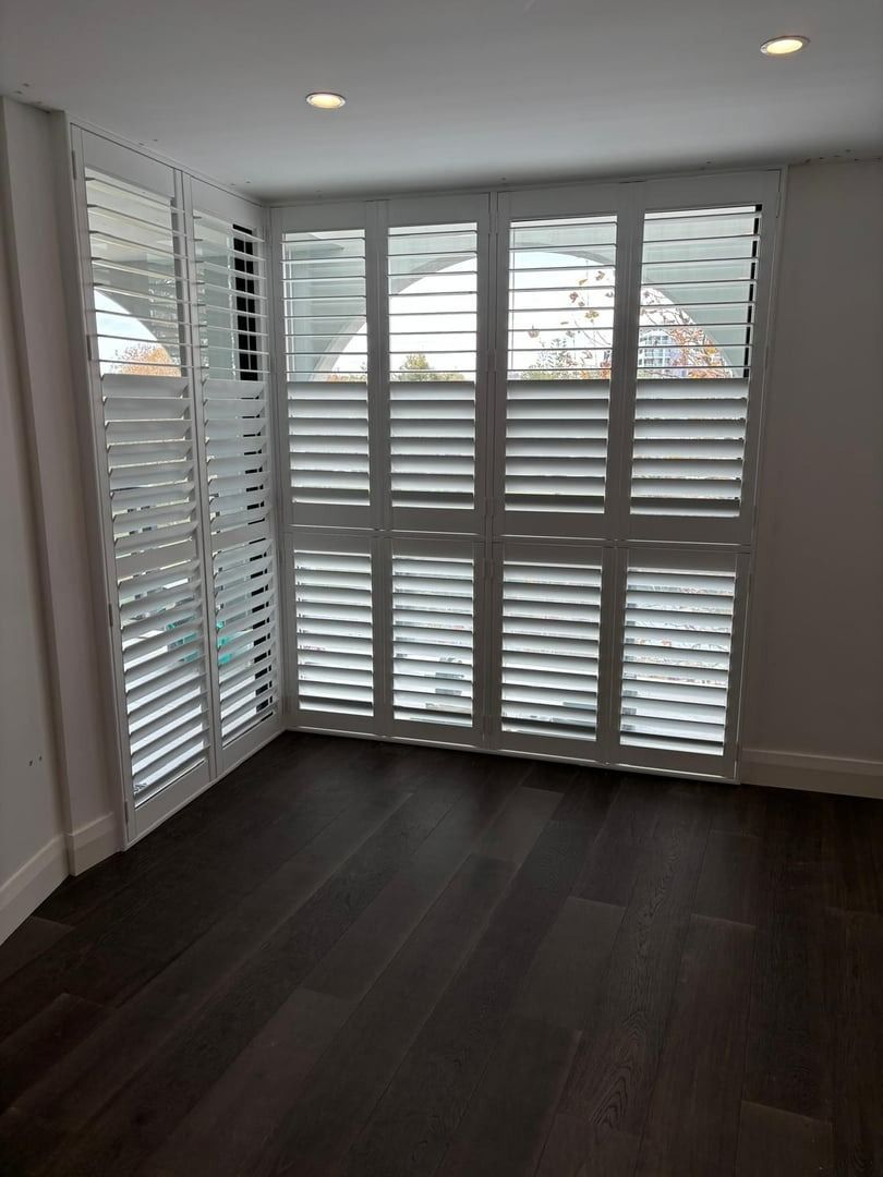 Plantation shutters installed in an empty room with dark wood floors, white plantation shutters, and recessed ceiling lights in Perth, WA.