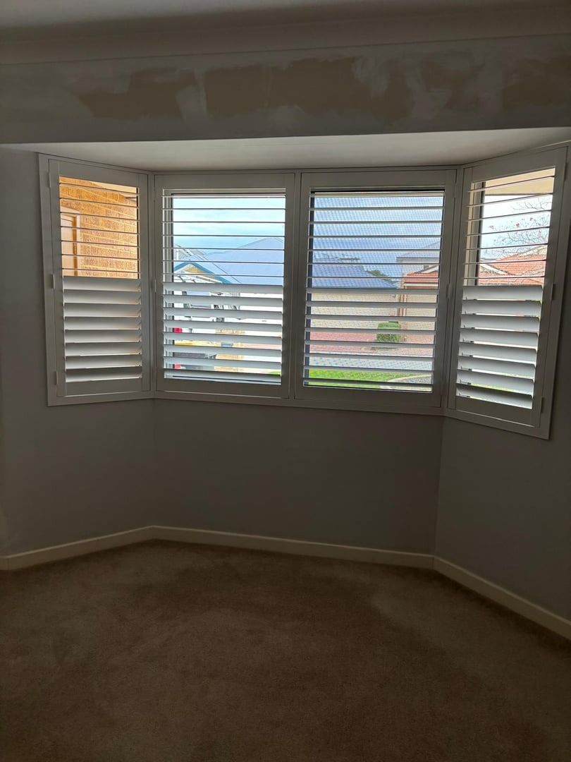 Plantation shutters installed in an empty room with a bay window and white plantation shutters overlooking the outside in Joondalup, WA.