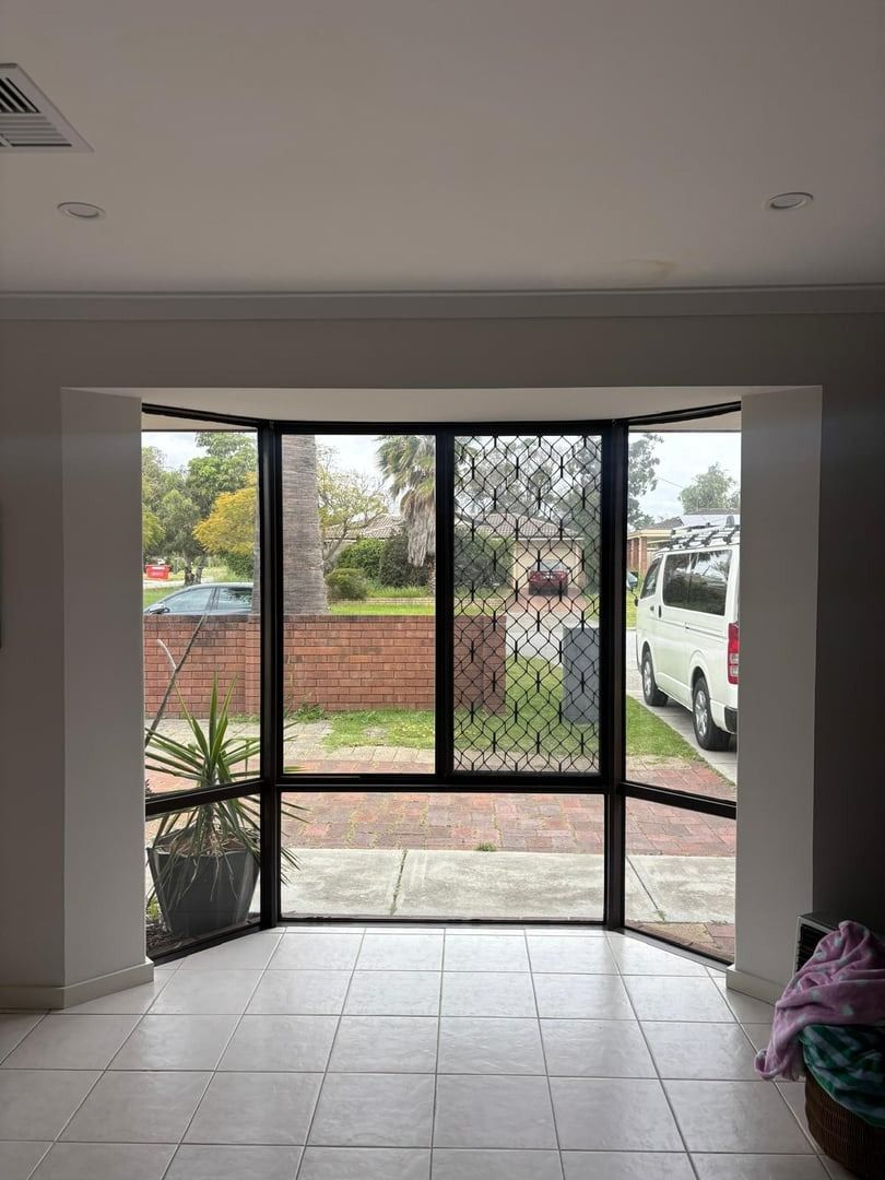 Plantation shutters installed in an interior view of a tiled room opening to a fenced yard through black security screens in Joondalup, WA.