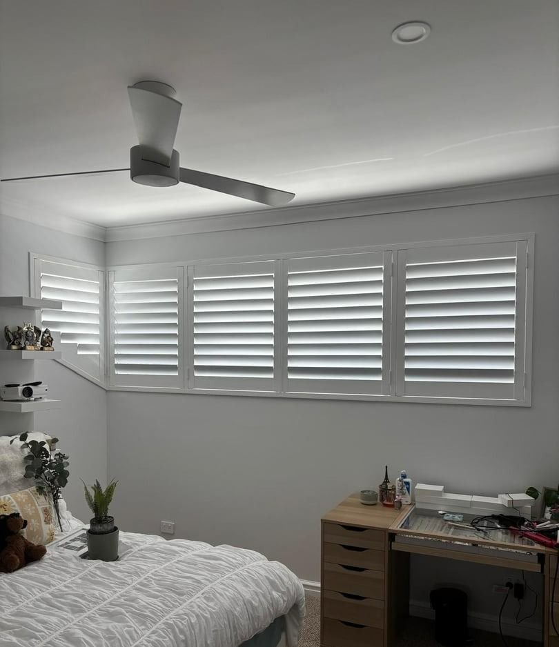 Bright white room with a round window, ceiling fan, and floor cushions by the wall